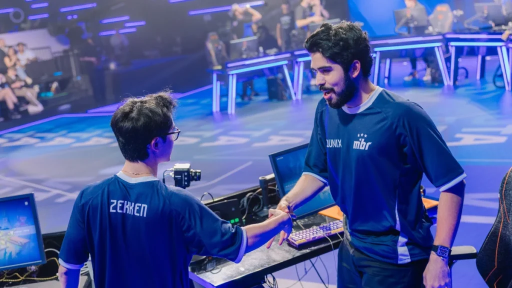O papel do Duelista no Valorant: como criar espaço nos bombsites e vencer duelos de mira Aspas e Zekken se cumprimentam durante evento de esports, usando uniformes do MIBR em palco de competição de VALORANT.